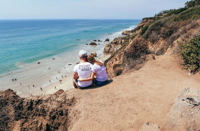 High angle view of couple sitting on cliff against sea