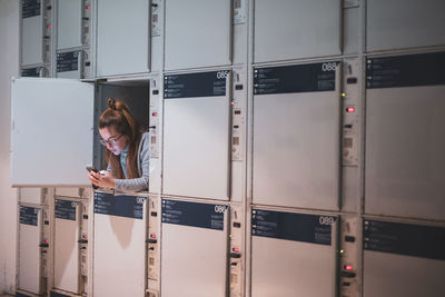 Young woman using phone in locker