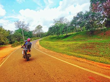 Rear view of man riding bicycle on road against sky