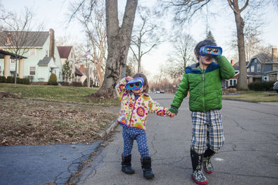 Siblings holding hands while looking through binoculars while playing on road