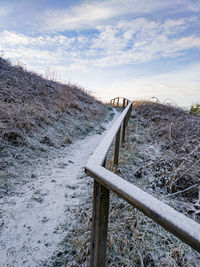 Snow covered railing on hill against cloudy sky