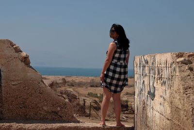 Full length of woman standing by wall against clear sky