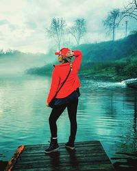 Rear view of woman with hand behind head standing on jetty during foggy weather