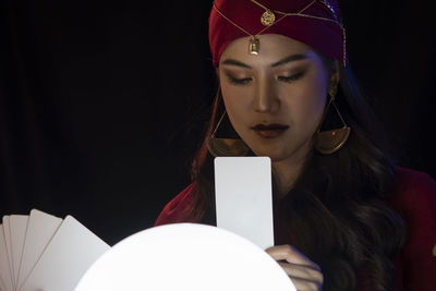 Female fortune teller looking at tarot card against black background