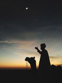 Silhouette man photographing against sky at sunset