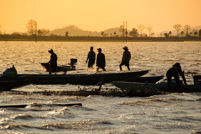 Silhouette people on boat at sea against sky during sunset