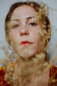 Close-up portrait of young woman seen through dried plant