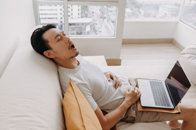 High angle view of exhausted man with laptop sitting home