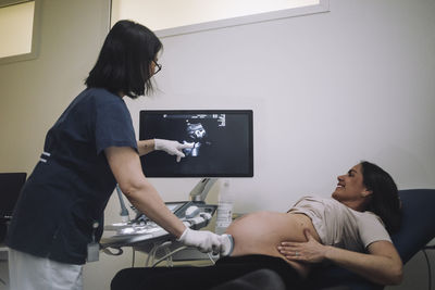 Female gynecologist pointing at screen while doing ultrasound of pregnant woman in medical clinic