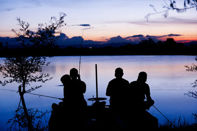 Silhouette people sitting by lake against sky during sunset