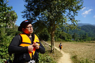 Thoughtful man wearing life jacket while standing against trees