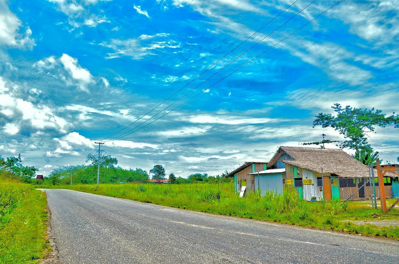 architecture, road, built structure, building exterior, the way forward, transportation, blue, house, landscape, sky, countryside, day, solitude, rural scene, cloud, country road, outdoors, tranquility, tranquil scene, cloud - sky, remote, long, empty road, green color, diminishing perspective, farm, power line, leading