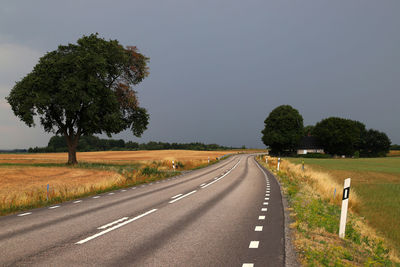 Road by trees on field against sky