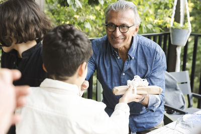 Smiling senior man giving gift to grandson during dinner party