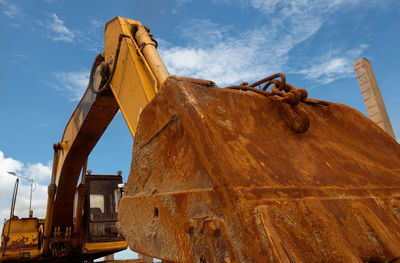 Closeup rusty metal bucket of old backhoe parked at construction site against blue sky. excavating