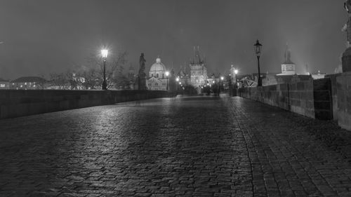 Illuminated street amidst buildings against sky at night