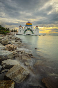 Scenic view of temple at waterfront against cloudy sky
