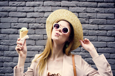 Portrait of woman holding ice cream against wall