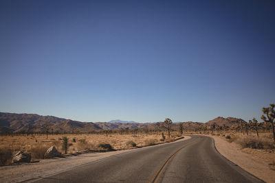 Road by landscape against clear blue sky