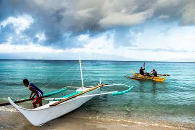 People and boat at beach against cloudy sky