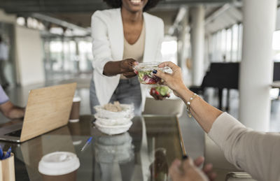 Businesswoman giving salad box to senior colleague at desk