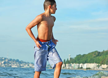 Shirtless boy walking in sea against sky