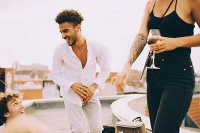 Happy young man dancing and enjoying drinks with friends on terrace at party