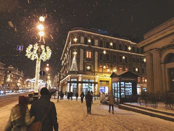 People on illuminated street amidst buildings in city at night