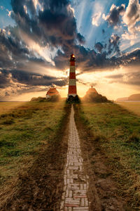 Lighthouse amidst field against sky during sunset