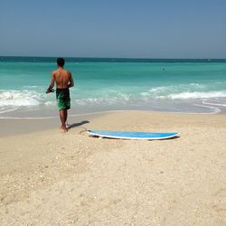 Rear view of shirtless boy on beach against sky