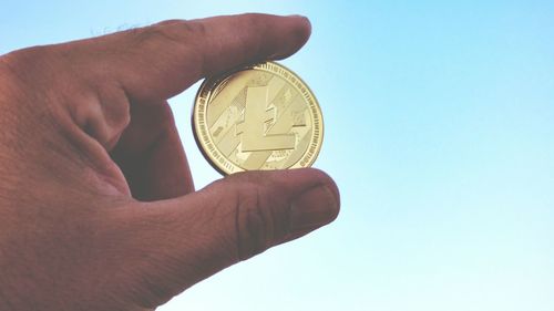 Close-up of hand holding coin against the sky