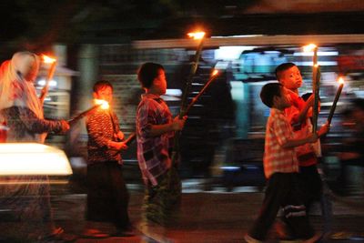 Side view of people standing on illuminated road at night