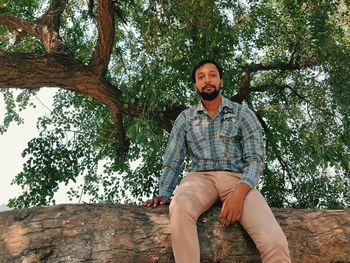 Low angle view of young man sitting on tree trunk