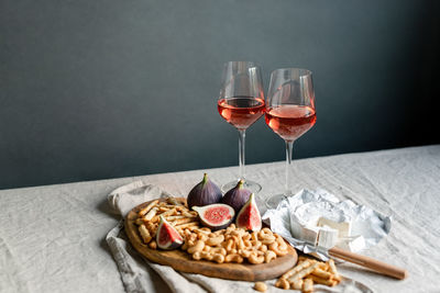 Rose wine with ripe figs, camembert cheese and cashews on a table indoors.