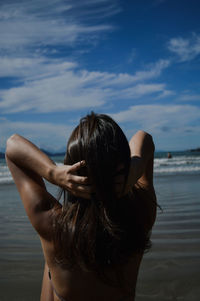 Rear view of woman sitting at beach against sky