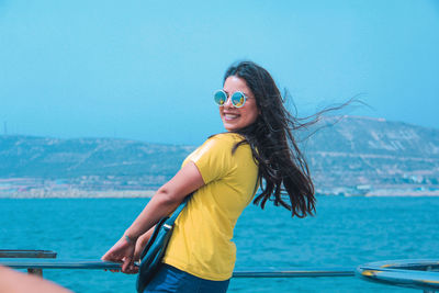 Portrait of smiling woman in sunglasses standing against sea