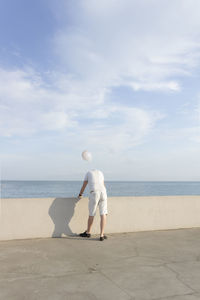 Rear view of man standing at beach against sky