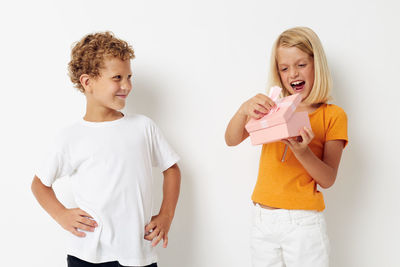 Girl with gift box standing with brother against white background