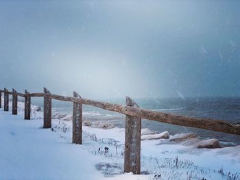 Fence on snow covered land against sky