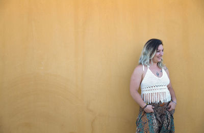 Portrait of happy spanish girl standing against yellow wall