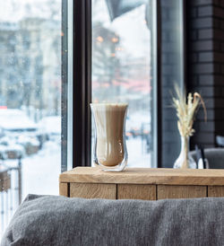 Coffee with milk foam in glass cup on wooden table in cafe or coffeehouse.