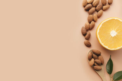 Raw almond kernels in wooden spoon on beige background, green herb leaves, half of orange fruit