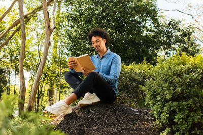 Young man sitting on book against trees