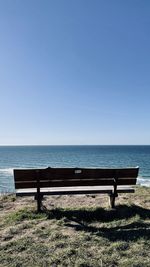 Empty bench by sea against clear sky