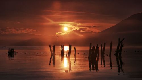 Silhouette of wooden posts on beach against sky during sunset