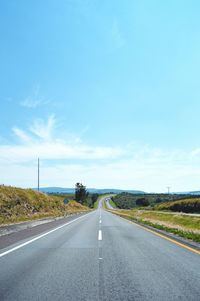 Road amidst field against blue sky