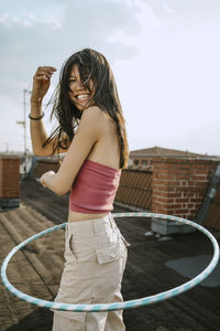 Side view of cheerful woman spinning hoola hoop on rooftop