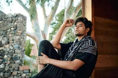 Young man looking away while sitting on stone wall