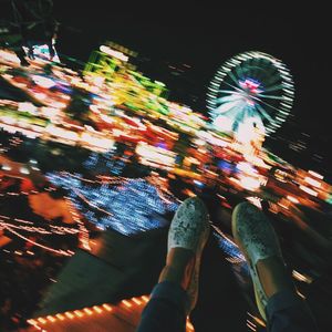 Low angle view of hands holding illuminated ferris wheel against sky at night