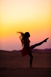 Silhouette woman walking on street against sky during sunset